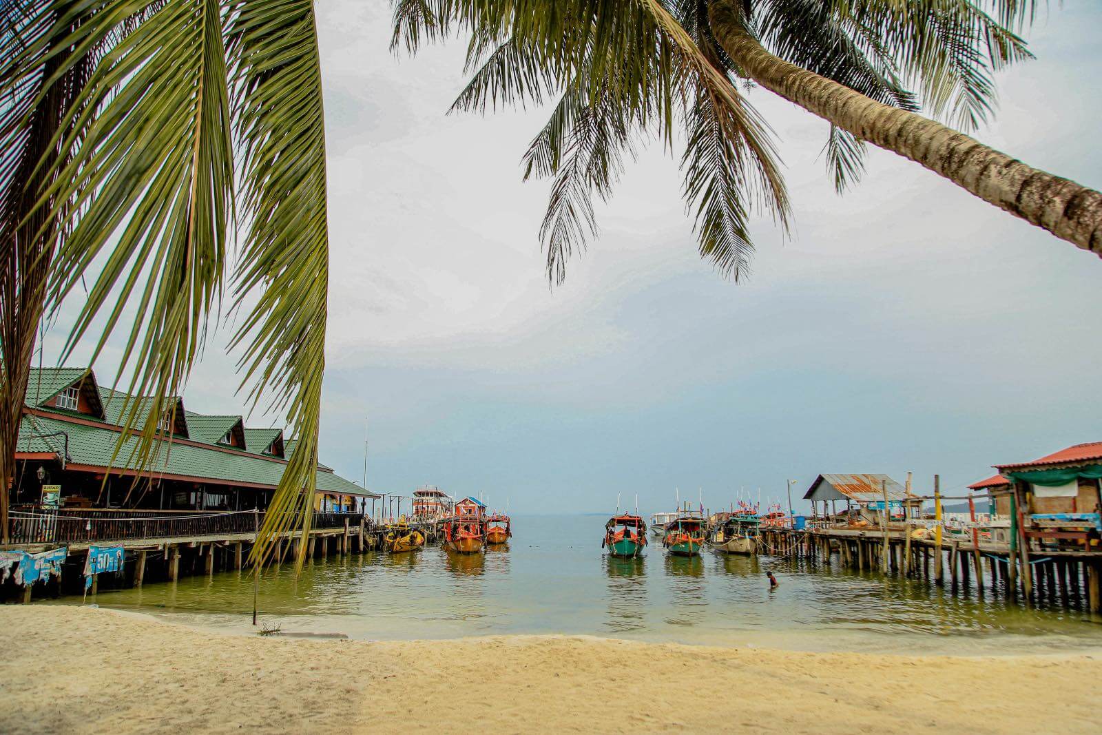 Palm tree on a beach looking into a boat harbor in Koh Rong, Cambodia