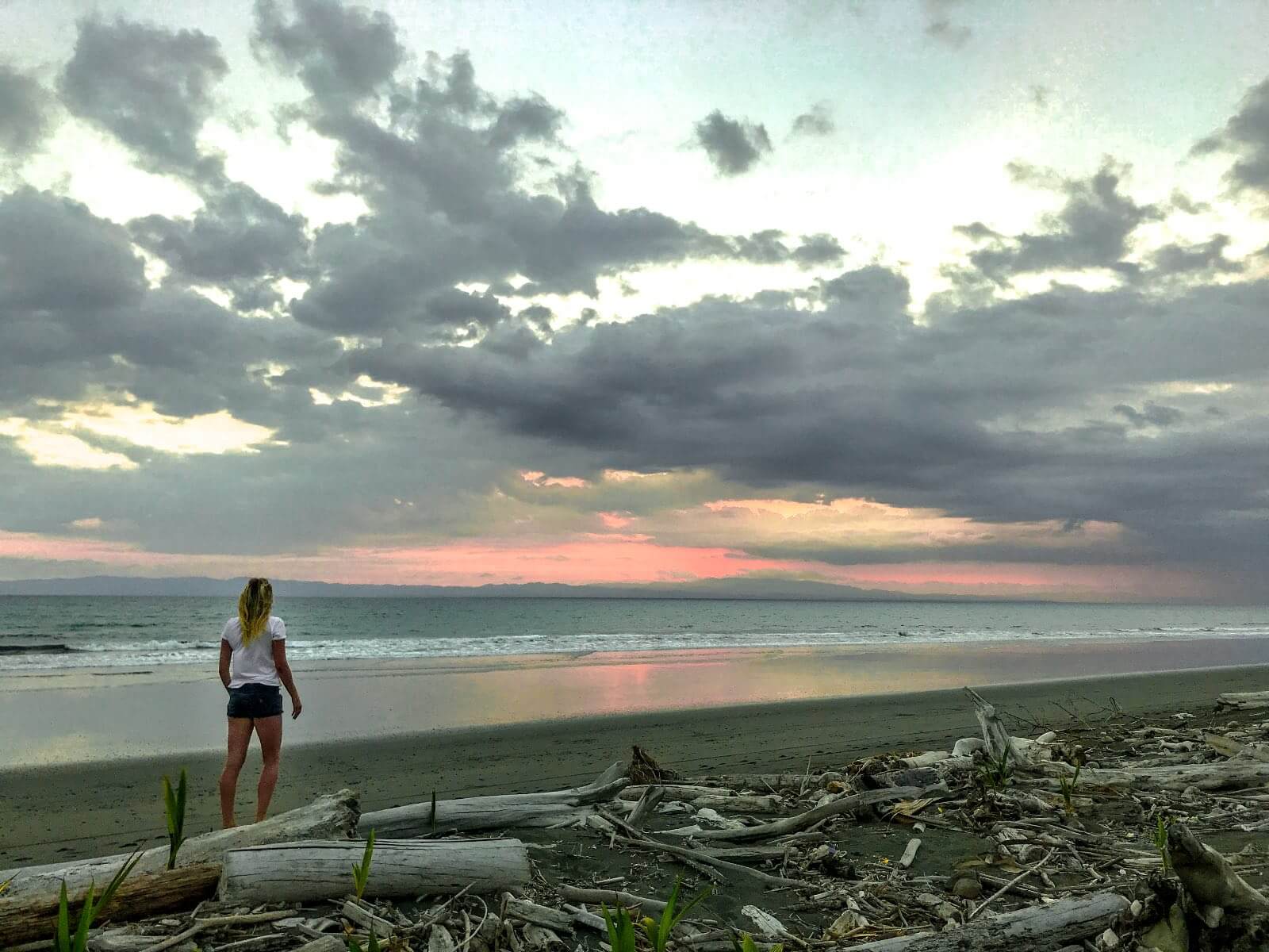 Jess standing on the beach at sunset in Costa Rica Girl standing on a driftwood beach in Zancudo
